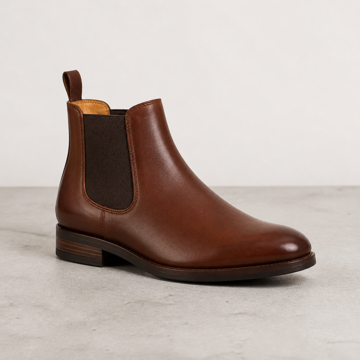 Une paire de bottines Chelsea marron pour homme en cuir lisse avec empiècements élastiques posée dans un studio au fond neutre.